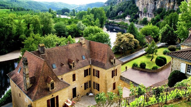 Un bâtiment historique doté d’une cour intérieure, entouré d’une végétation luxuriante et bordé par une rivière.