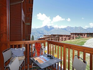 A wooden balcony with a table, chairs, and a view of mountains.