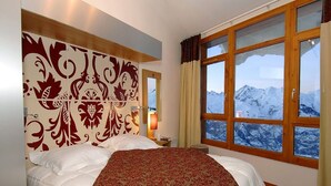 Ein Hotelzimmer mit einem großen Bett, einem dekorativen Kopfteil, einem Nachttisch, einer Lampe und einem Fenster mit Blick auf die Berge.
