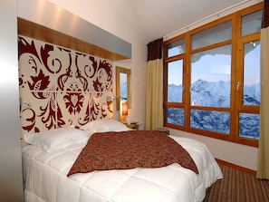 Ein Hotelzimmer mit einem großen Bett, einem dekorativen Kopfteil, einem Nachttisch, einer Lampe und einem Fenster mit Blick auf die Berge.