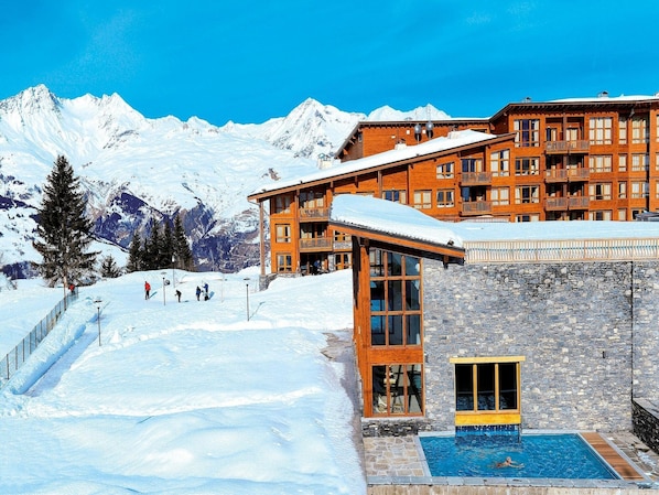 A wooden building with a pool, surrounded by snow-covered mountains.