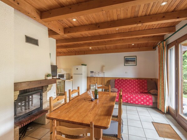 A cozy room with a wooden table and chairs, a sofa, a fireplace, and a kitchen area. - Chalet in Lotharingen near Forest & Ski Lift (La Bresse)