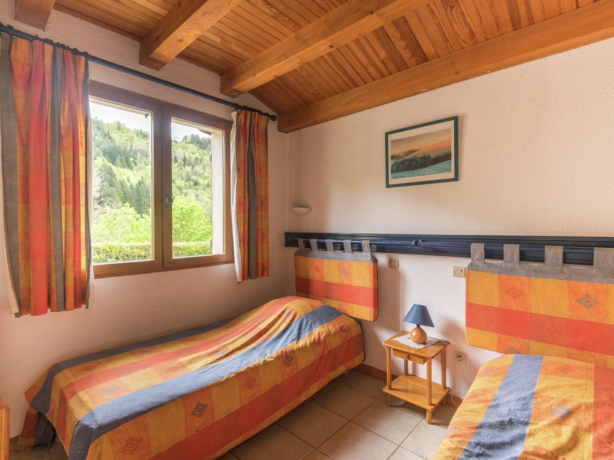 Une chambre avec deux lits, une fenêtre avec des rideaux, une lampe et un tableau au mur.