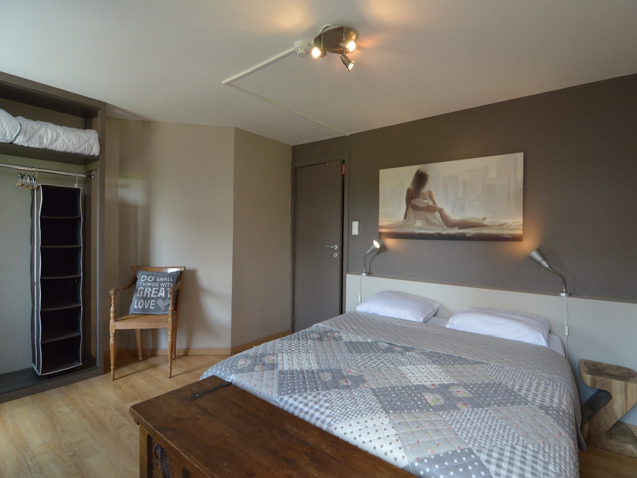 A bedroom with a bed, a chair, a desk, a wardrobe, and a painting on the wall.