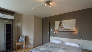 Une chambre à coucher avec un lit, une chaise, un bureau, une armoire et un tableau accroché au mur.