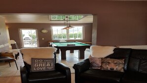 Un salon comprenant une table de billard, deux fauteuils en cuir avec des coussins moelleux et un canapé en cuir noir.