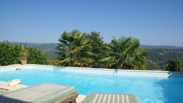 Ein Pool mit Liegestühlen und Palmen, umgeben von einer gebirgigen Landschaft.