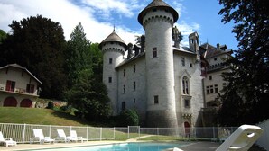 Un château doté d’une tour ronde, d’une piscine et de chaises longues blanches.