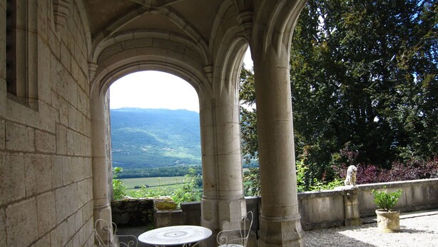 Une terrasse extérieure agrémentée d’une arche en pierre, d’une table ronde et de deux chaises.