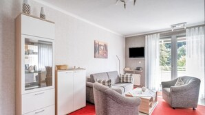 Un salon moderne avec une moquette rouge, un canapé gris, un meuble blanc et un téléviseur fixé au mur.
