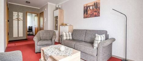 A living room with a grey sofa, a smaller armchair, a wooden coffee table, and a red patterned carpet.