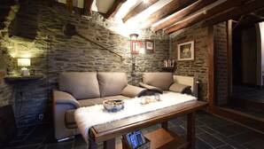 A cozy room with stone walls, wooden beams, a sofa, a table with a basket, and a lamp. - Gite at the Calm way in the Center (Bastogne-Rachamps)