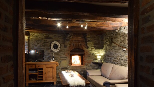 A cozy room with a stone fireplace, a wooden cabinet, a sofa, and a table with a bottle and glasses. - Gite at the Calm way in the Center (Bastogne-Rachamps)