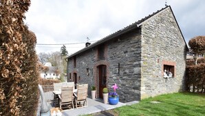 A stone building with a patio, a table with chairs, and a statue of sheep. - Gite at the Calm way in the Center (Bastogne-Rachamps)
