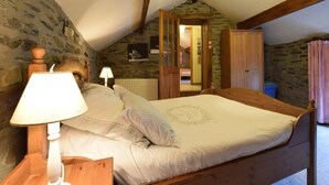 A bedroom with a wooden bed, a nightstand, a lamp, and a stone wall. - Gite at the Calm way in the Center (Bastogne-Rachamps)