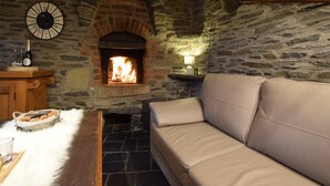 A cozy room with a stone fireplace, a wooden table with a bottle, and a beige sofa. - Gite at the Calm way in the Center (Bastogne-Rachamps)