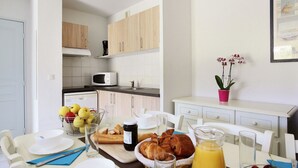 A modern kitchen with wooden cabinets, a microwave, and a dining area with breakfast items. - Coastal Stay for Groups (Saint-Aygulf)