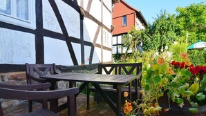 Tavolo e sedie di legno all'aperto, con vista su un edificio a graticcio e un giardino fiorito.