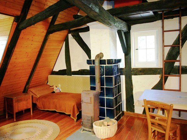 A cozy attic bedroom with wooden beams, a bed, a dresser, and a large window. - Traditionelles Ferienhaus in Hessen mit Garten (Willingshausen)