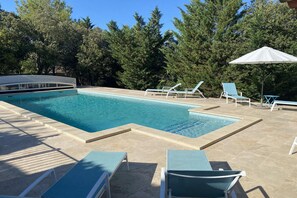 A swimming pool with lounge chairs and a covered area.