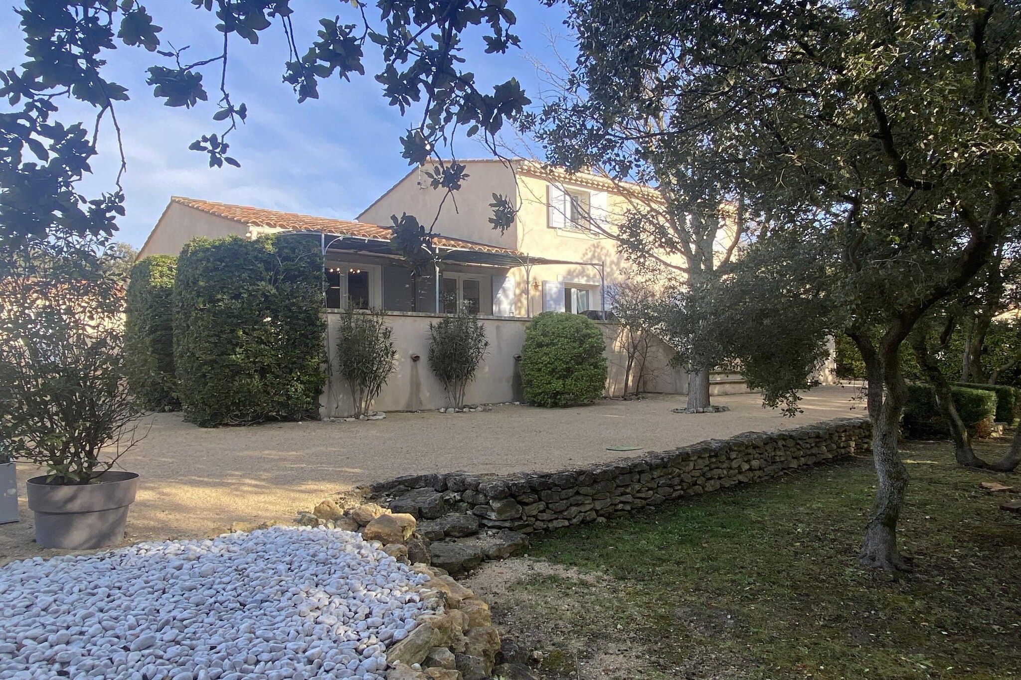 Una casa con un muro de piedra, camino de grava y un pequeño arroyo.
