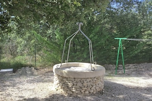 A stone well with a metal frame, surrounded by gravel and trees. - Inviting Villa with Swimming Pool (SAUMANE-DE-VAUCLUSE)