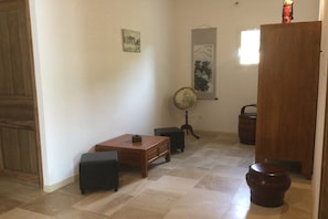 A room with a wooden table, a black ottoman, a globe on a stand, and a wooden cabinet.