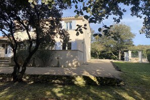 A building with a stone base and a flat roof, surrounded by trees and a grassy area.