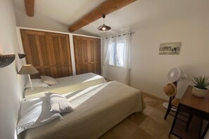 A bedroom with a bed, a bedside table, a lamp, a window with curtains, a fan, and a plant.
