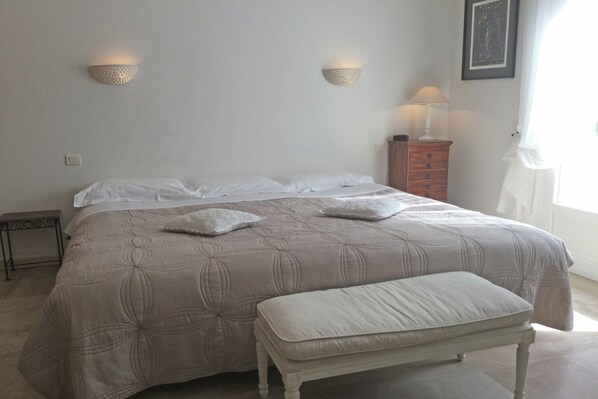 A bedroom with a bed, a bench, two wall-mounted lights, a nightstand, and a window.