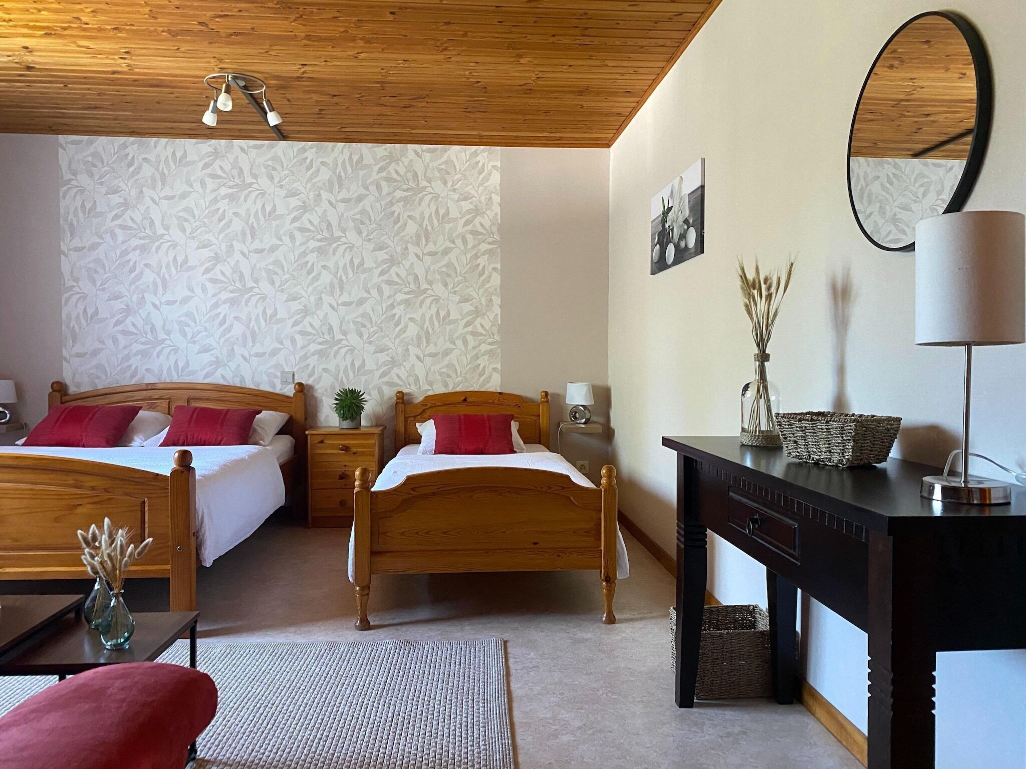 Une chambre d’hôtel avec deux lits en bois, un bureau avec une lampe, un miroir et un mur recouvert d’un papier peint à motifs floraux.