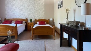 A hotel room with two wooden beds, a desk with a lamp, a mirror, and a wall with a floral wallpaper pattern.