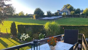 A patio with a table set for two, overlooking a well-maintained garden and a house in the background.