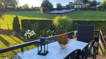 A patio with a table set for two, overlooking a well-maintained garden and a house in the background.