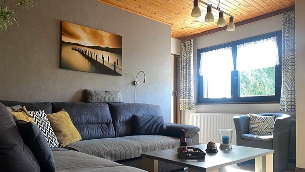 A modern living room with a sofa, a coffee table, and a window with patterned curtains.