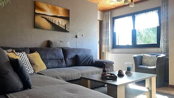A modern living room with a sofa, a coffee table, and a window with patterned curtains.