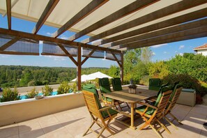 An outdoor patio with a wooden table and chairs, a view of a swimming pool, and a covered area with a pergola. - Charming villa in Rouzède with private garden (Ecuras - Rouzède)