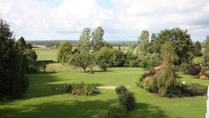 Een verzorgd grasveld met bomen en een klein gebouw, waarschijnlijk een gastenverblijf of vakantiehuisje, omringd door een hek.