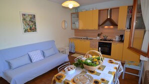Un salon chaleureux avec un canapé, une table à manger recouverte d’une nappe à motifs de tournesols et une cuisine avec des meubles jaunes.