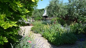 Un jardin avec un chemin en briques, diverses plantes et une structure blanche en arrière-plan.