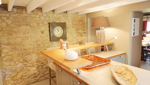 A kitchen with a stone wall, a wooden countertop, a clock, and a lamp. - Holiday Home in Ardennes near Chimay Abbey (Nismes Viroinval)