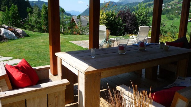 Une table en bois, des chaises et une vue sur un paysage verdoyant, avec des montagnes en arrière-plan.