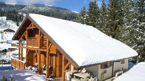 Un chalet en bois doté d’un balcon, entouré d’arbres couverts de neige et avec une montagne en arrière-plan.