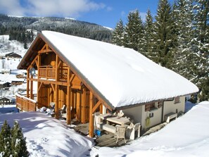 A wooden chalet with a balcony, surrounded by snow-covered trees and a mountain in the background. - Chalet in Les Gets with Ski-In/Ski-Out Access (Les Gets)
