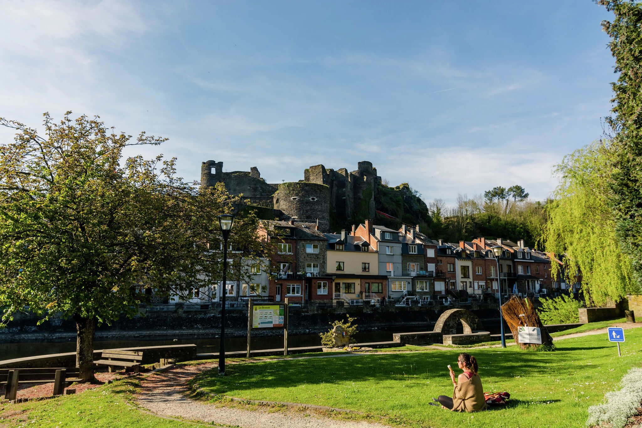 Eine historische Burg mit Blick auf einen Fluss, mit einem Park im Vordergrund und Wohngebäuden im Hintergrund.