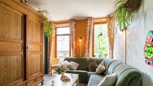 A cozy living room with a green sofa, wooden furniture, and a window with curtains.