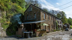 A stone building with a balcony, outdoor seating, and a car parked nearby.