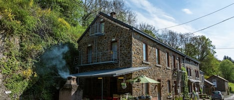 A stone building with a balcony, outdoor seating, and a car parked nearby.
