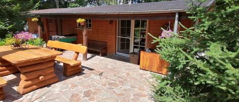 A wooden cabin with a stone patio, wooden furniture, and potted plants.