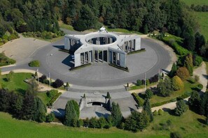 Een rond gebouw met een centrale koepel, omgeven door een aangelegd gebied met bomen en een verharde weg.